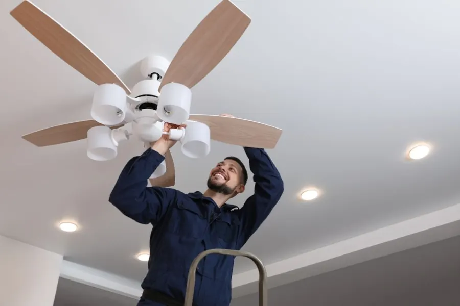 Stock photo: an electrician on a stepladder fitting a ceiling fan with lights.