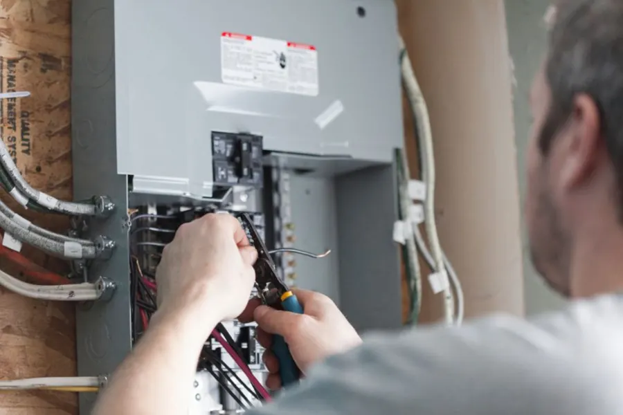 Stock photo: a hand with a tool inside an open electrical panel, wires running along the wall.