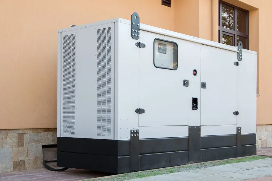 Stock photo: a large white backup generator in a metal cabinet beside a house wall.