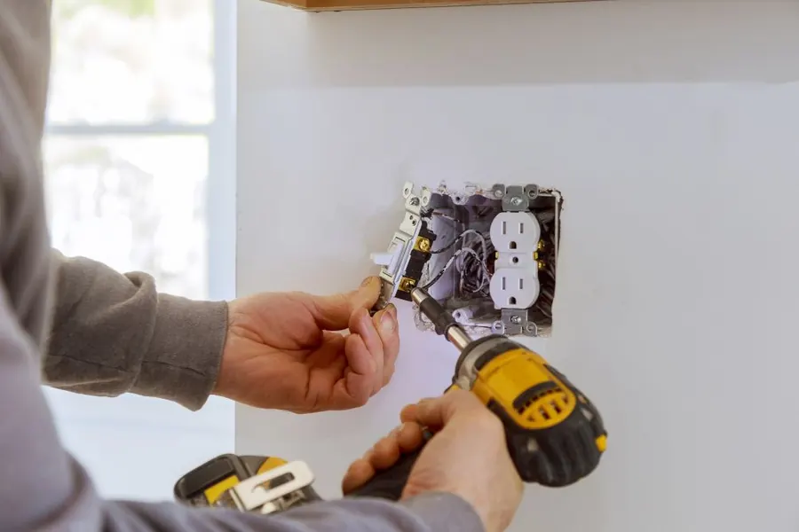 Stock photo: hands fitting an outlet into a wall box with a cordless drill.
